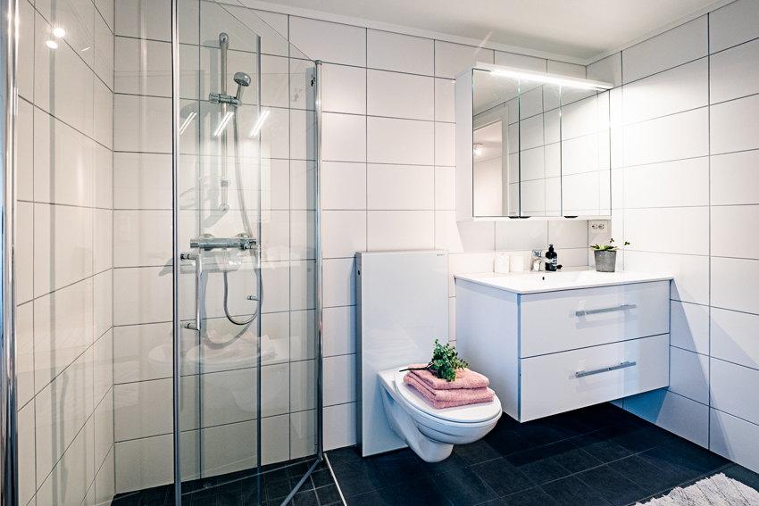 Badet har servant i moderne innredning med skuffer, dusjhjørne og vegghengt toalett