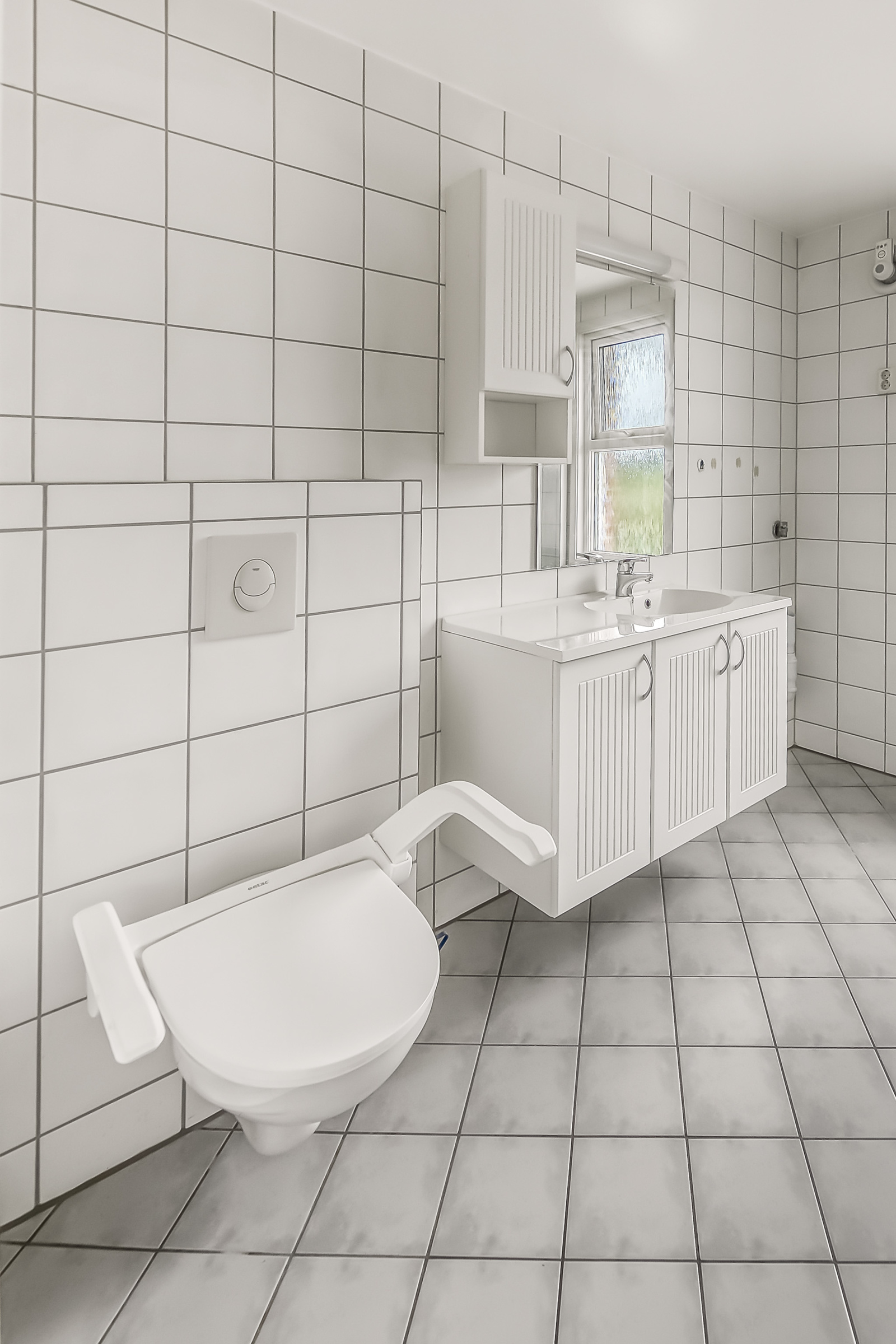 Badet har dusjkabinett, servant i innredning, speil, høyskap, vegghengt toalett og opplegg for vaskemaskin