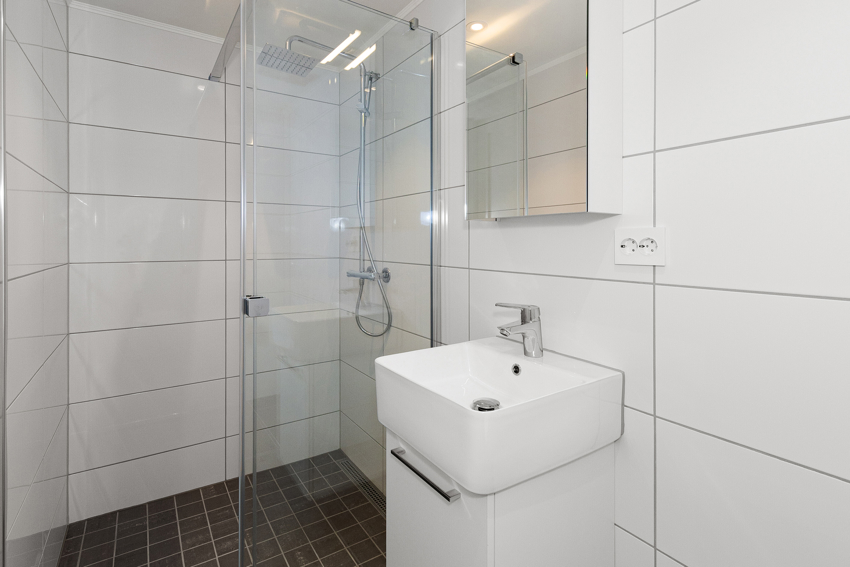 Bad nr 2 med dushjørne med foldedører, servant, speil og vegghengt toalett.