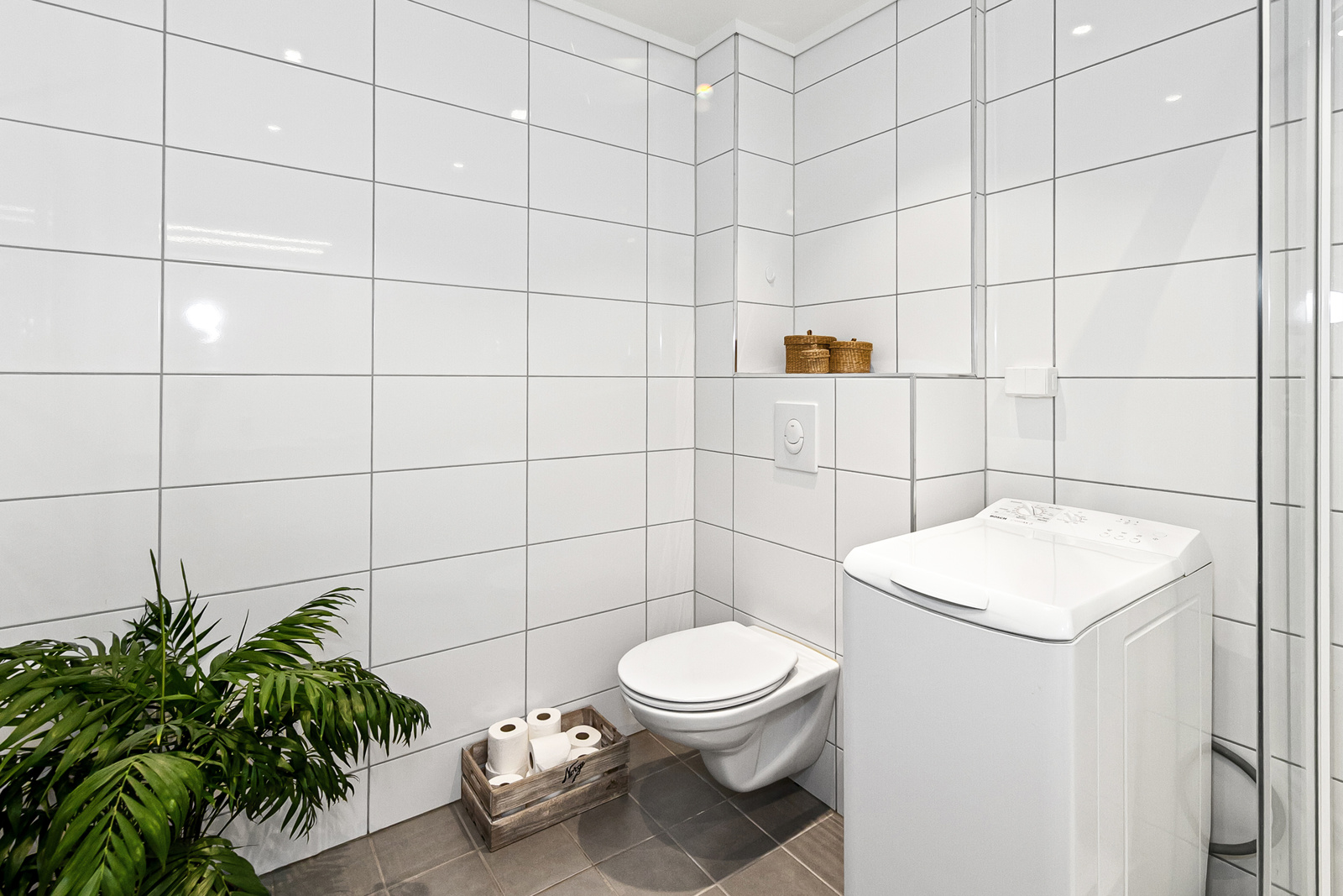 Badet har vegghengt toalett, dusjkabinett, servant i moderne innredning med skuffer, speil og opplegg for vaskemaskin