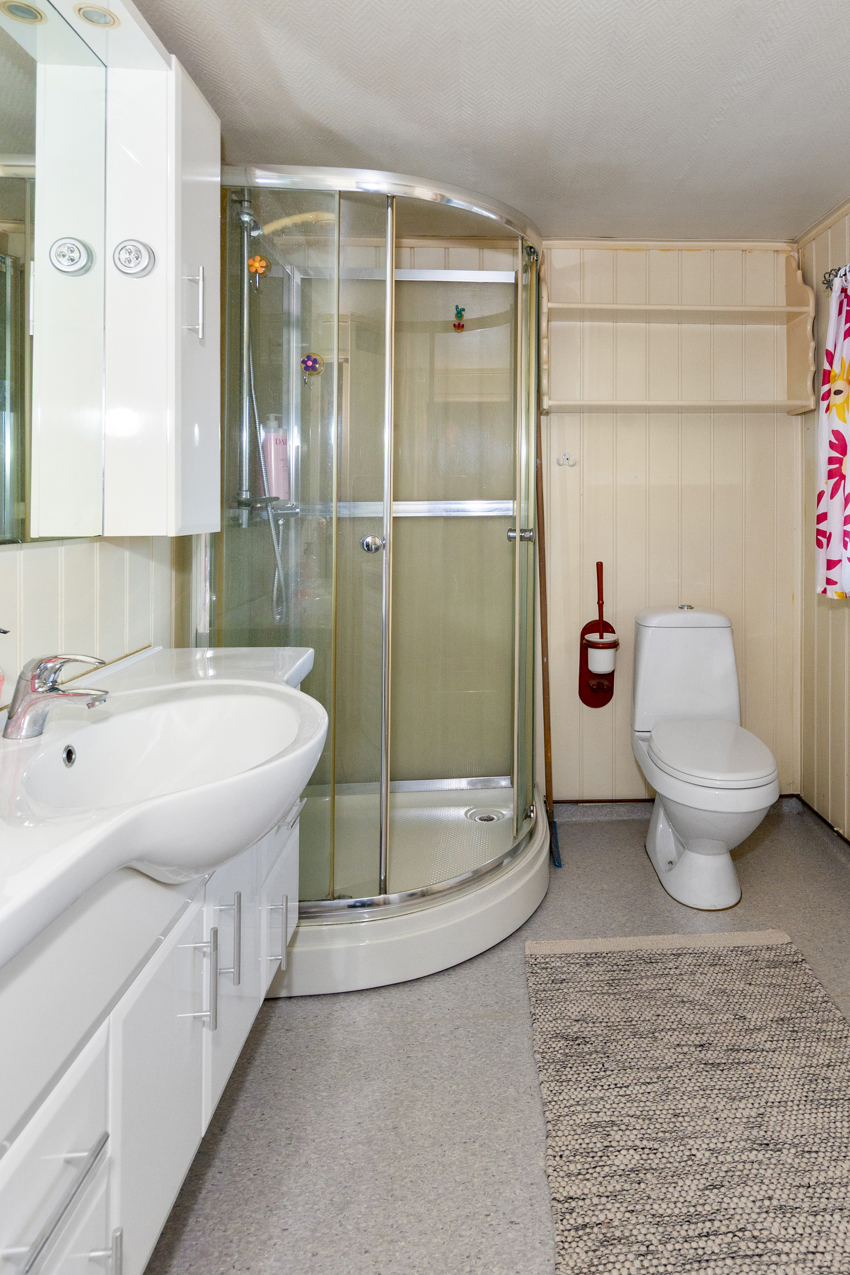 Baderom med gulvstående toalett og dusjkabinett. 