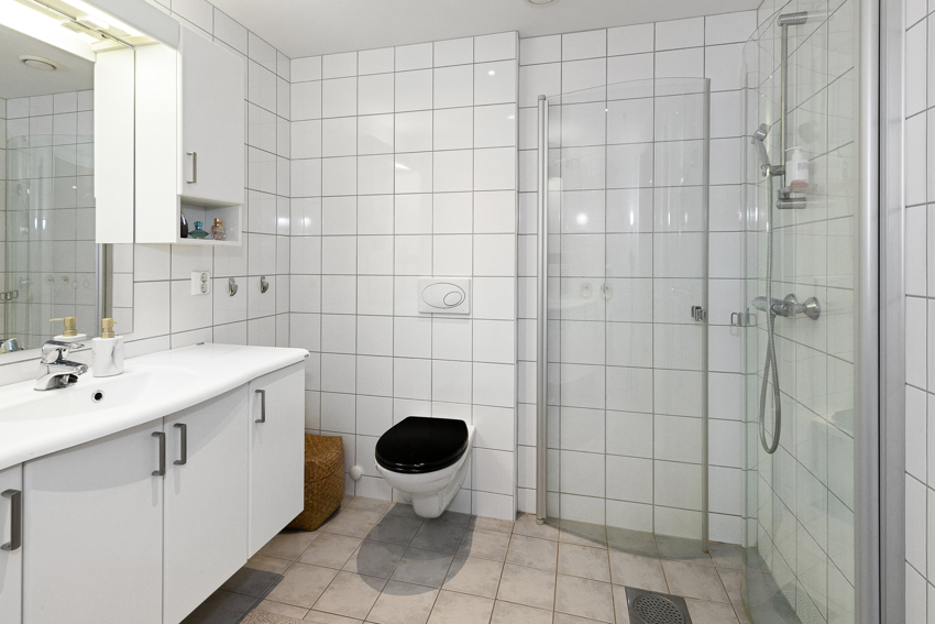 Innredningen består av heldekkende servant, et veggmontert toalett og dusjhjørne med foldedører i glass.