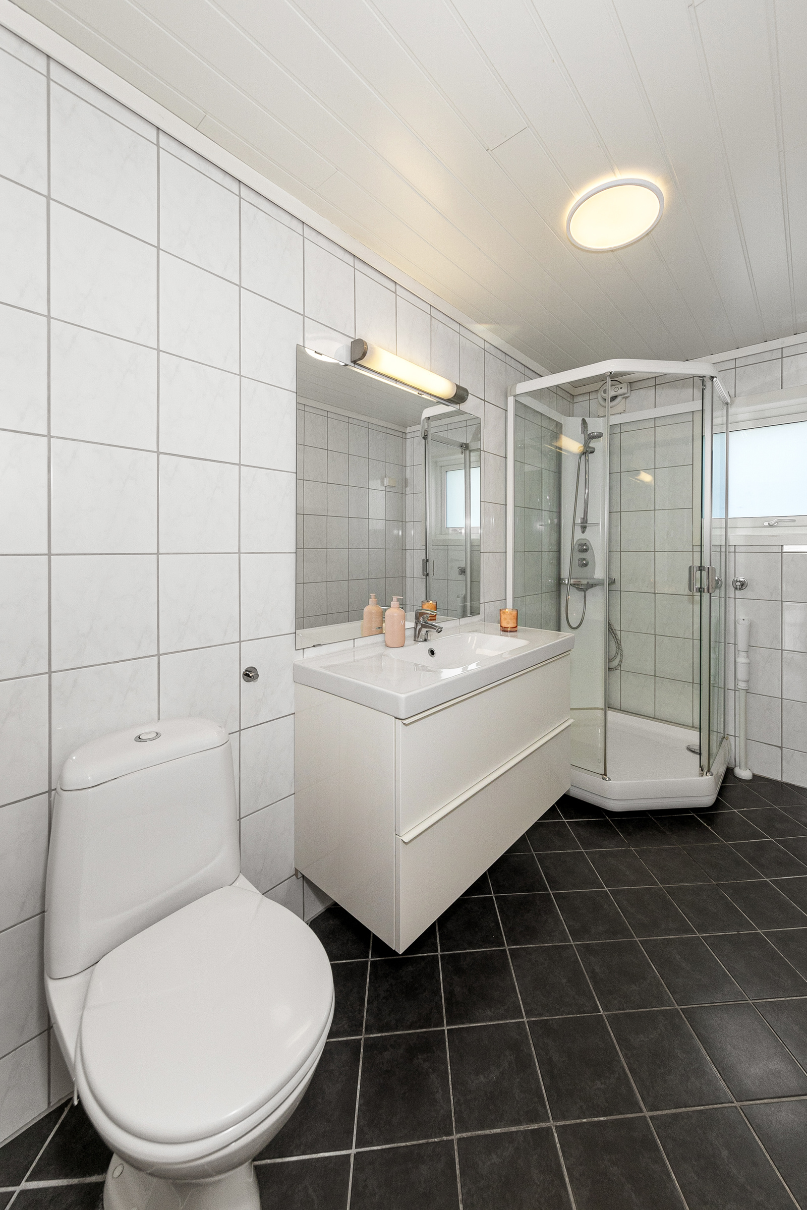 Badet har dusjkabinett, servant i moderne innredning med skuffer, stort speil, toalett og opplegg for vaskemaskin