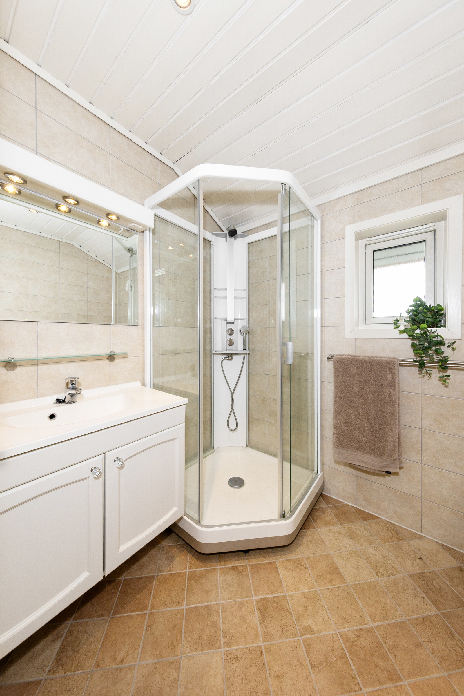 Badet har dusjkabinett, vegghengt toalett, servant i innredning samt opplegg for vaskemaskin