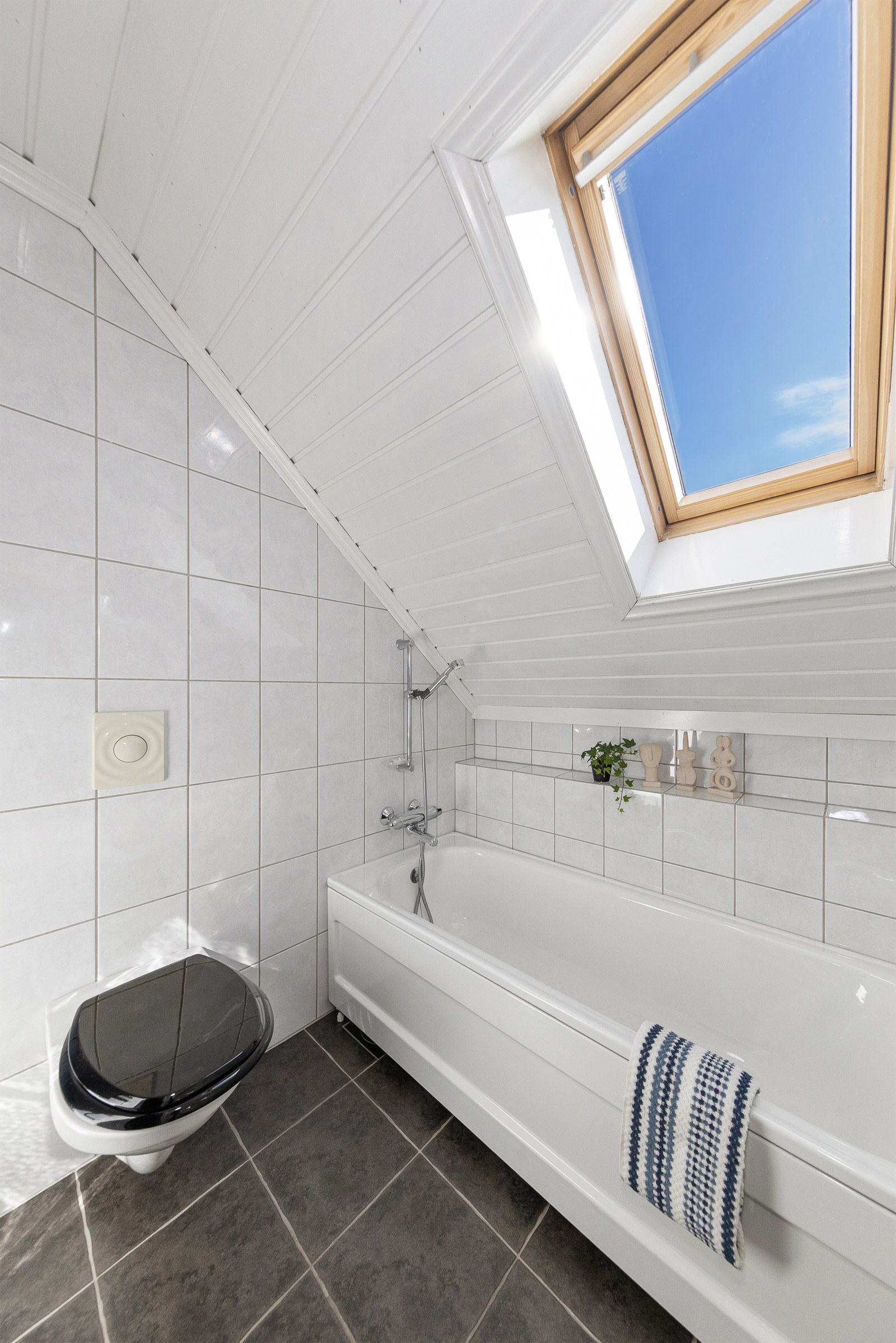 Badet har badekar, vegghengt toalett og servant i innredning samt høyskap 