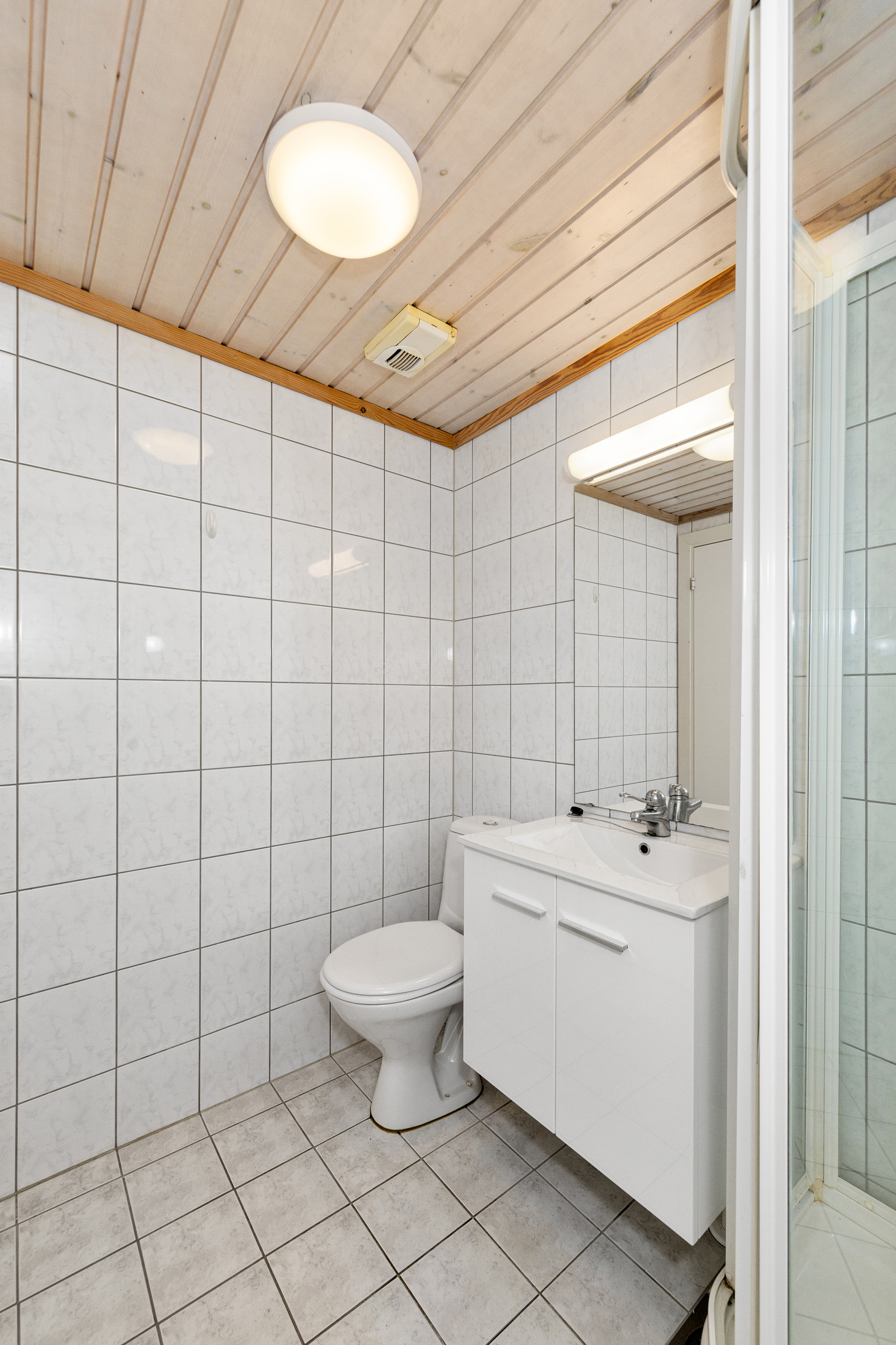 Badet har dusjkabinett, servant i innredning, speil, toalett og opplegg for vaskemaskin