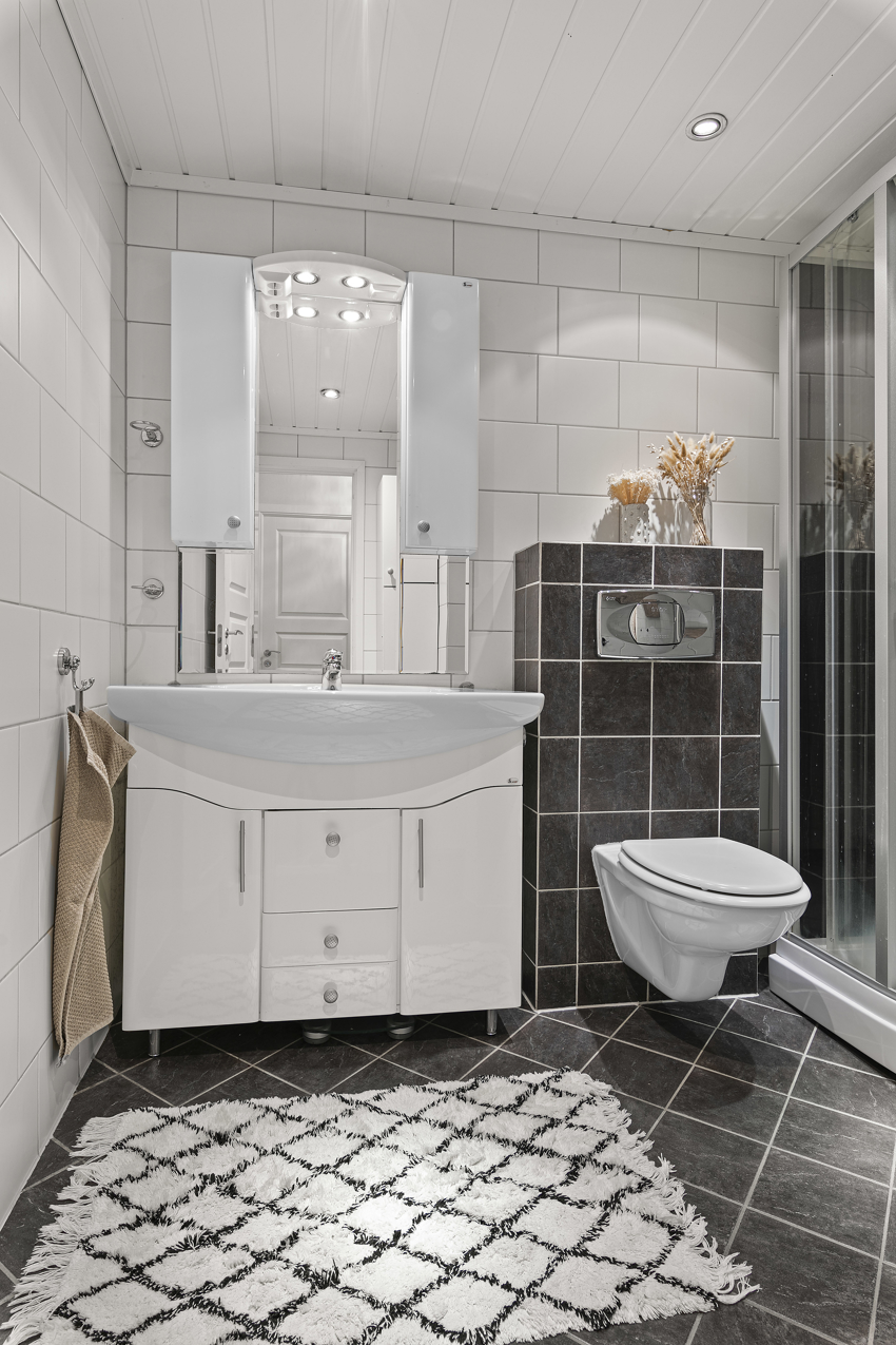 Badet har dusjkabinett (nytt i 2018), vegghengt toalett, servant i innredning med overskap og speil samt høyskap