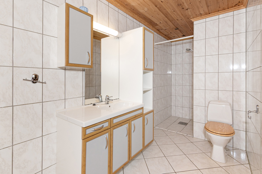 Vegghengt høyskap og servantskap. Speil, skap og overlys med stikkontakt på vegg over servant. Badekar og dusjnisje. 