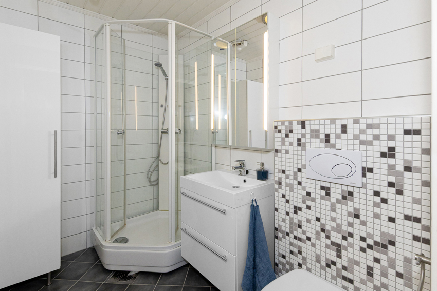 Badet har dusjkabinett, servant i innredning, høyskap, speilskap m/innfelt lys samt vegghengt toalett