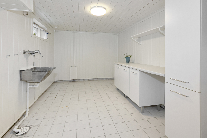 Romslig og praktisk vaskerom i kjeller med utslagsvask og kjekk innredning med benk og oppbevaring for orden i sakene