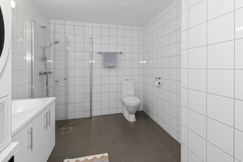 Badet har praktiske dusjdører som slås inn når dusjen ikke er i bruk, servant i innredning, toalett og opplegg for vaskemaskin/tørketrommel