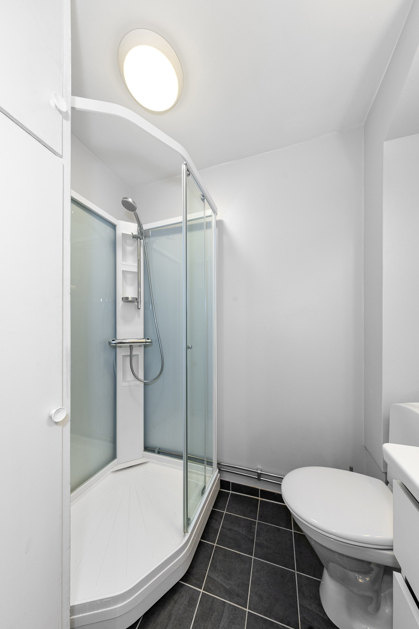 Badet har dusjkabinett, servant i innredning m/skuffer, toalett og plassbygd høyskap