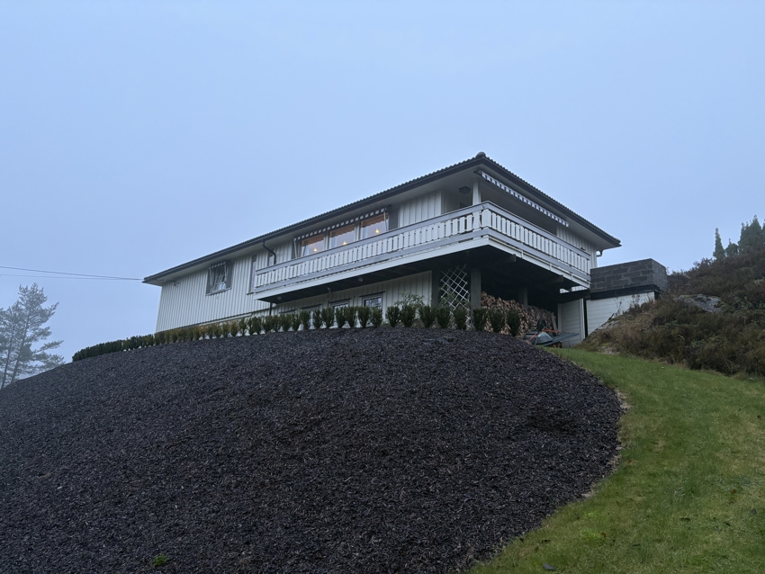 Pent opparbeidet hage med hekkplanter og bark i skråning.