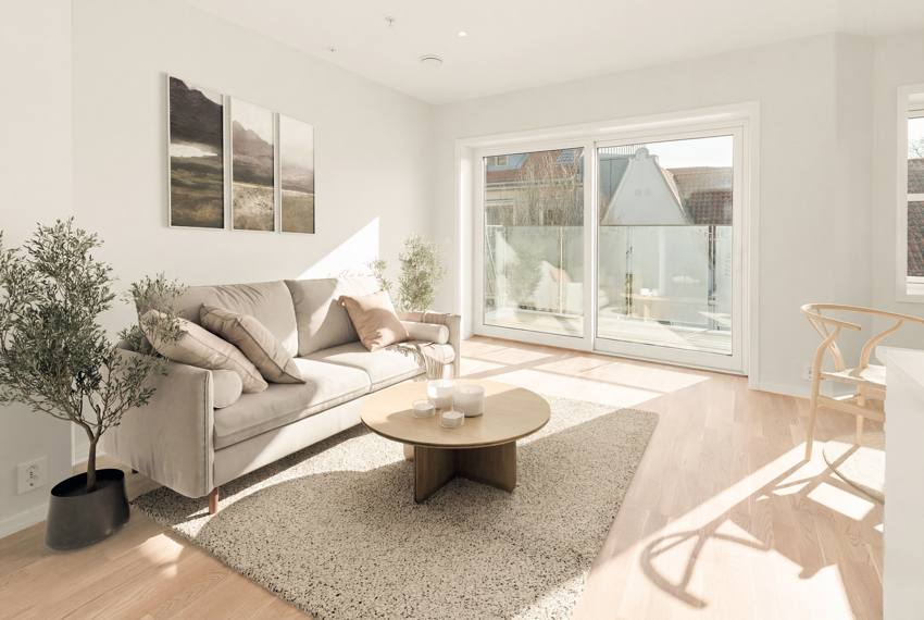 Stuen har en moderne og luftig atmosfære med skyvedør ut til balkong og utsikt mot nærområdet. (bildet er digitalt stylet).