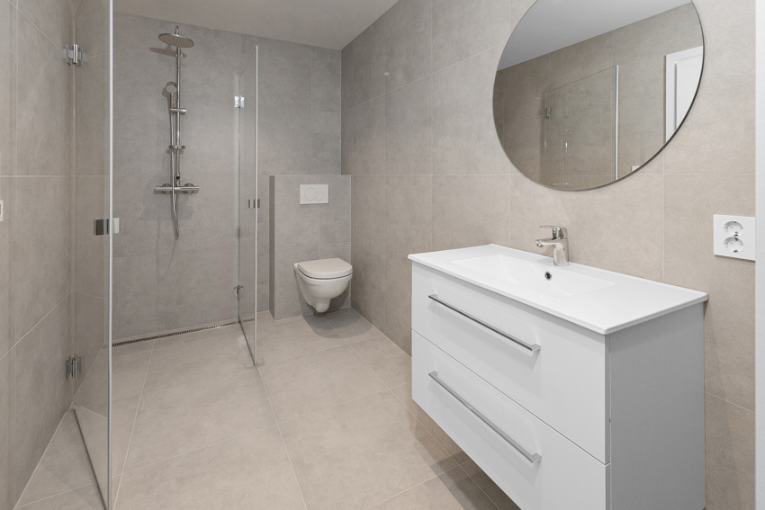 Leiligheten har et meget romslig bad med dusjhjørne og foldedører. Det er vegghengt toalett, servant med møbel og tidsriktig rundt speil. 