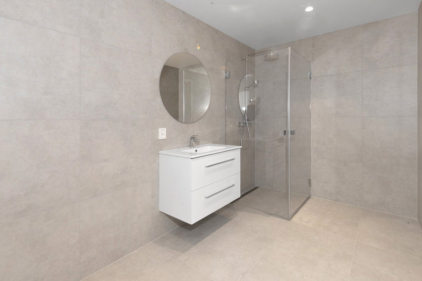 Badet har servant med møbel, moderne rundt speil og dusjhjørne med foldedører. 