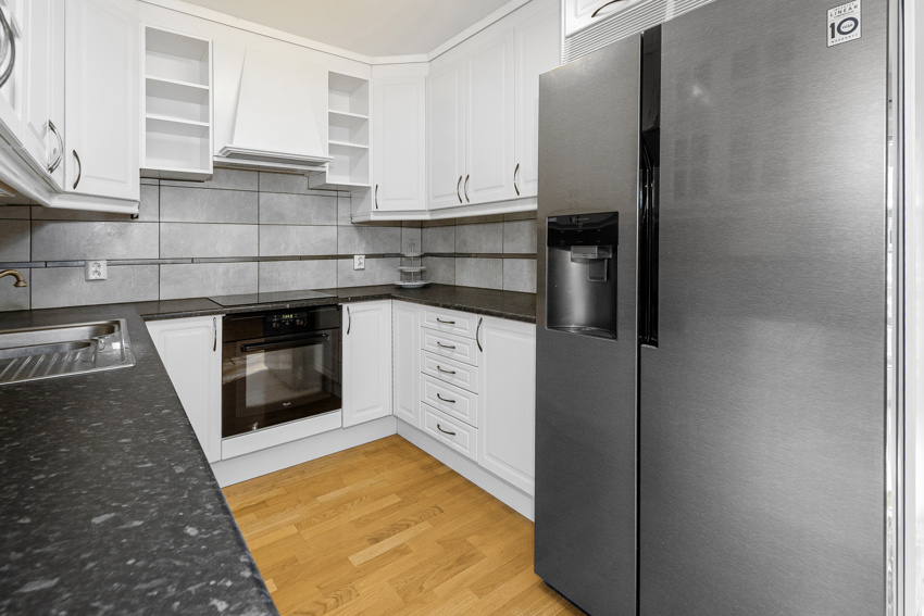 Pen kjøkkeninnredning med profilerte fronter og glass samt laminert benkeplate og flis mellom over- og underskap.