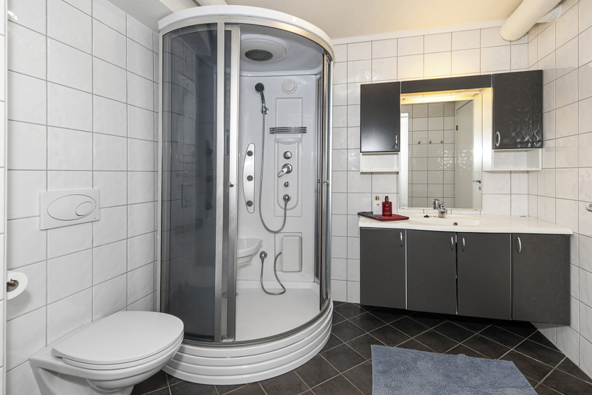 Stort og deilig bad/vaskerom med dusjkabinett, veggmontert toalett og innredning med skap og heldekkende servant.