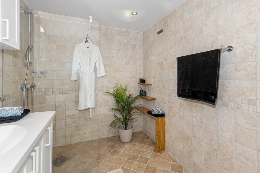 Badet inneholder dusjnisje med dusjdører, toalett og servantinnredning med underskap, overskap, speil og overlys med el-stikk.